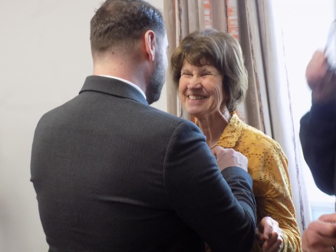 Anette recevant son insigne tout sourire, avec une personne de dos lui remettant