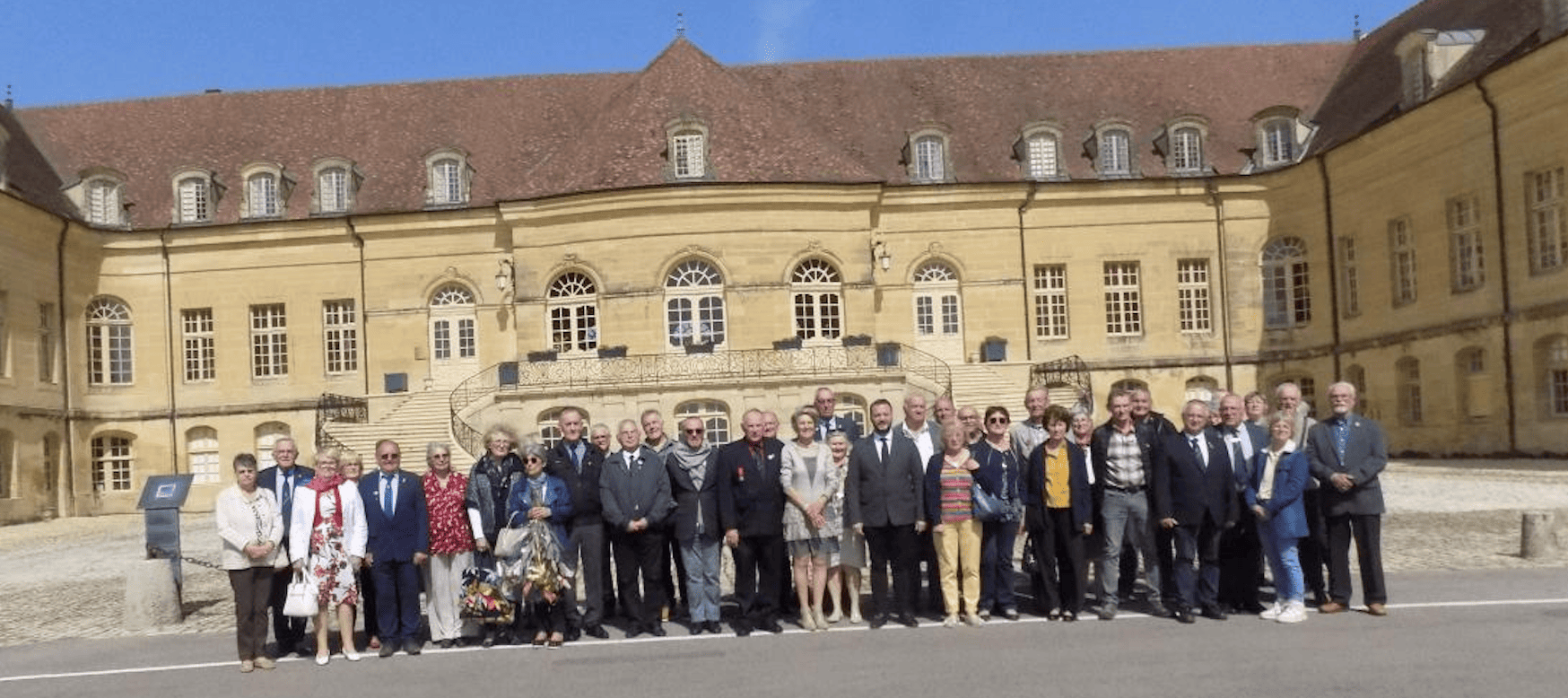 Photo de groupe d’une quarantaine de personnes posant devant le château de Saint-Rémy-en-Comté sous un ciel bleu, dans la cour du bâtiment historique aux façades beige clair et au toit en tuiles.